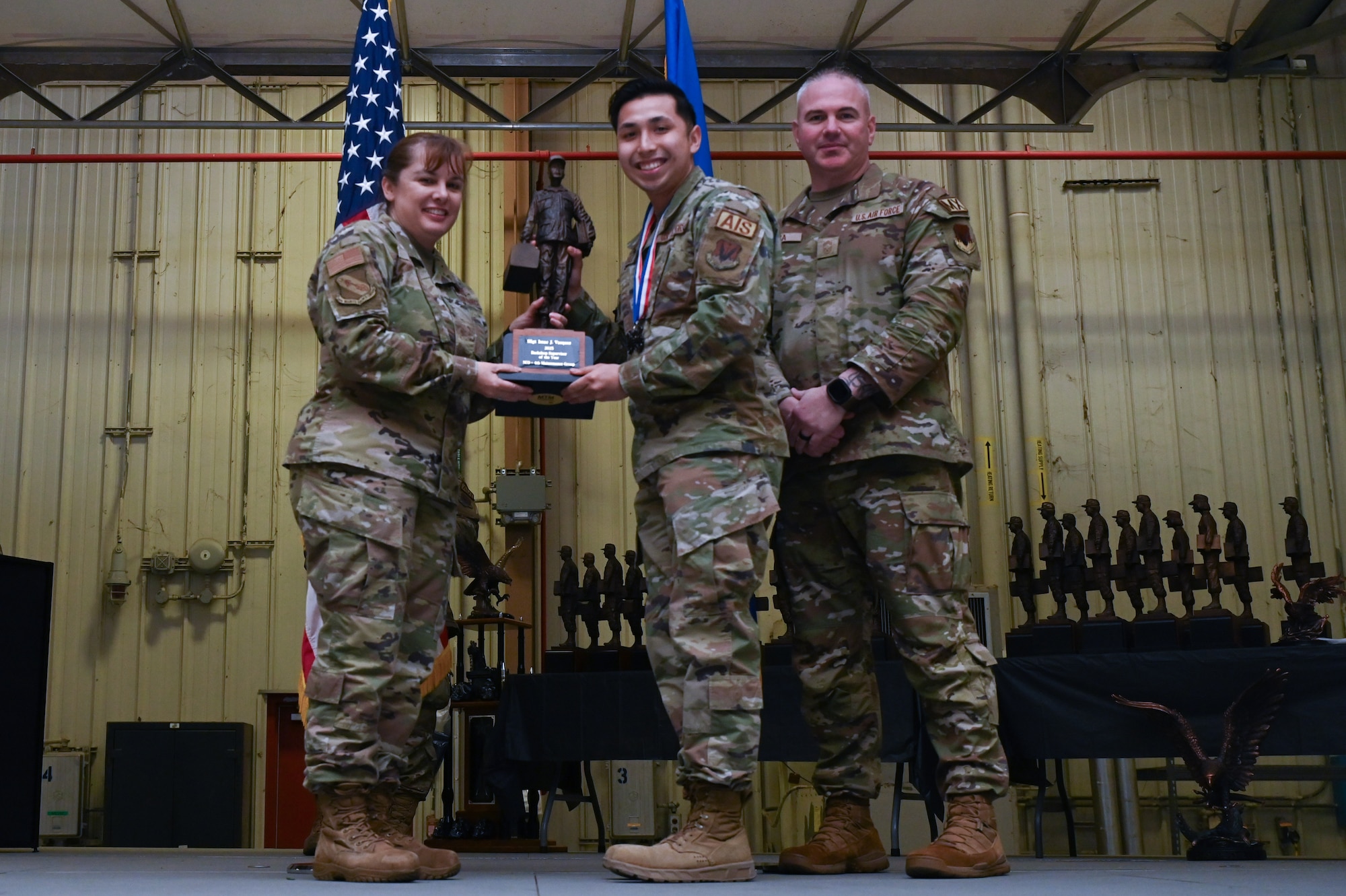 Staff Sgt. Isaac Vasquez, center, assigned to the 4th Component Maintenance Squadron, receives the Back-shop Technician of the Year award from Col. Kathryn Roman, 4th Maintenance Group commander and Chief Master Sgt. Michael Bylica, 4 MXG senior enlisted leader, during the 4 MXG Maintenance Person of the Year ceremony at Seymour Johnson Air Force Base, North Carolina, Mar. 08, 2024. The MPOY ceremony recognized 37 Airmen from multiple maintenance career fields and highlighted their accomplishments. (U.S. Air Force photo by Airman Rebecca Tierney)