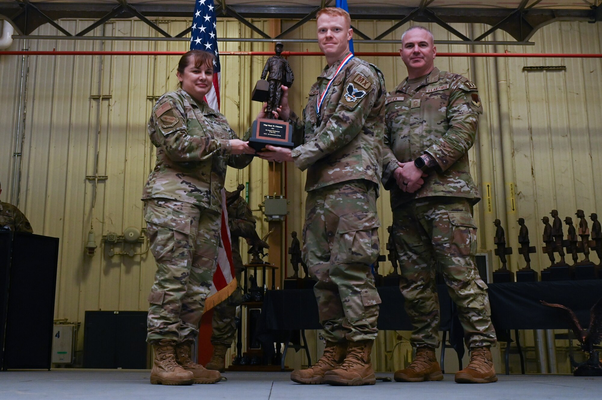 Tech. Sgt. Mark Clements, center, assigned to the 336th Fighter Generation Squadron, receives the Maintenance Support Professional of the Year award from Col. Kathryn Roman, 4th Maintenance Group commander and Chief Master Sgt. Michael Bylica, 4 MXG senior enlisted leader, during the 4 MXG Maintenance Person of the Year ceremony at Seymour Johnson Air Force Base, North Carolina, Mar. 08, 2024. The MPOY ceremony recognized 37 Airmen from multiple maintenance career fields and highlighted their accomplishments. (U.S. Air Force photo by Airman Rebecca Tierney)
