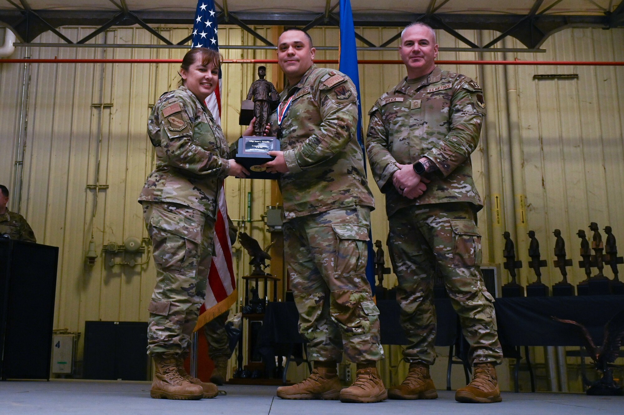 Master Sgt. Jason Jaramillo, center, assigned to the 333rd Fighter Generation Squadron, receives the Maintenance Support Professional of the Year award from Col. Kathryn Roman, 4th Maintenance Group commander and Chief Master Sgt. Michael Bylica, 4 MXG senior enlisted leader, during the 4 MXG Maintenance Person of the Year ceremony at Seymour Johnson Air Force Base, North Carolina, Mar. 08, 2024. The MPOY ceremony recognized 37 Airmen from multiple maintenance career fields and highlighted their accomplishments. (U.S. Air Force photo by Airman Rebecca Tierney)
