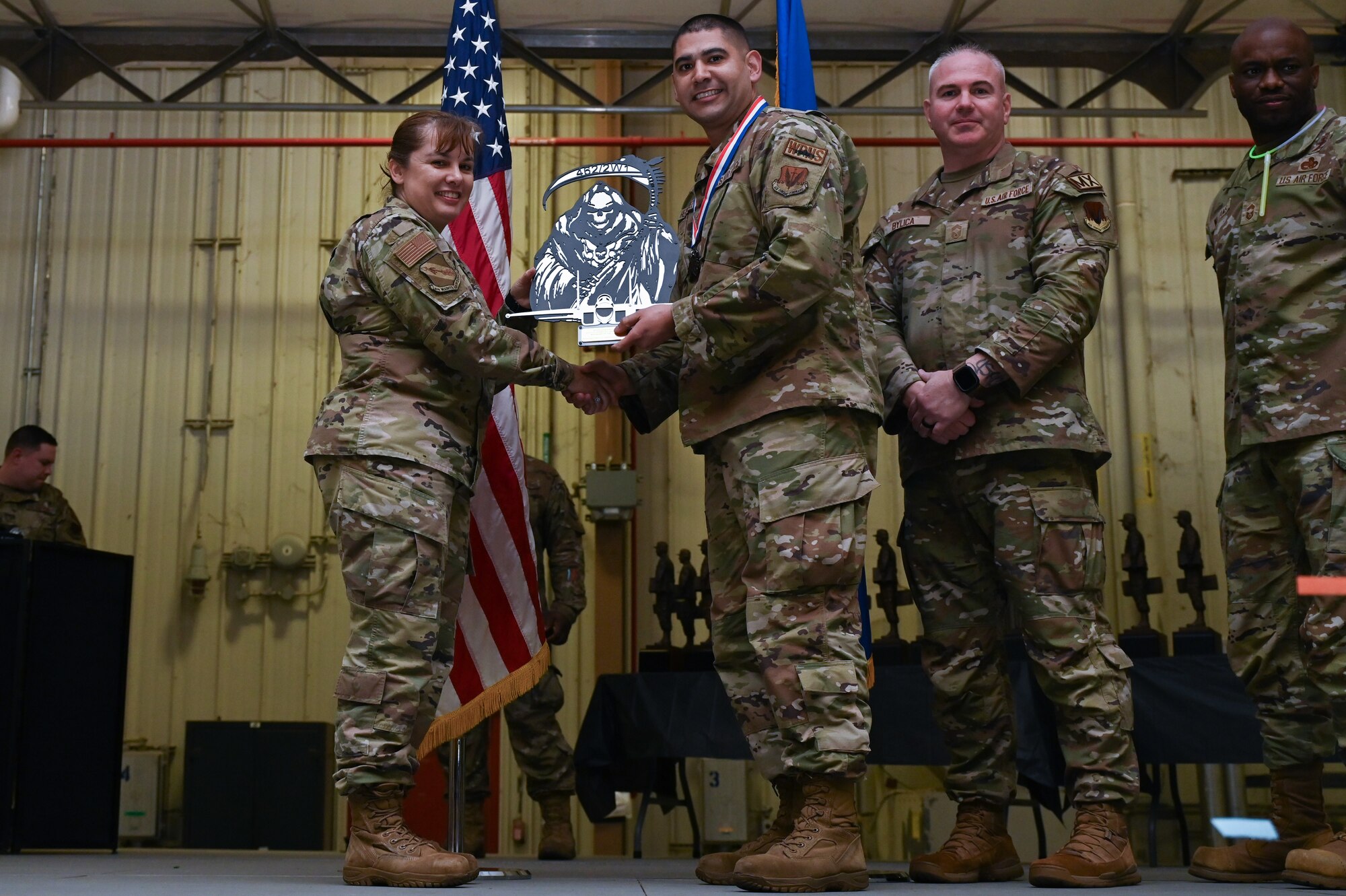Master Sgt. Eduardo Hernandez, center, assigned to the 4th Maintenance Operations Squadron, receives the Armament Manager of the Year award from Col. Kathryn Roman, 4th Maintenance Group commander and Chief Master Sgt. Michael Bylica, 4 MXG senior enlisted leader, during the 4 MXG Maintenance Person of the Year ceremony at Seymour Johnson Air Force Base, North Carolina, Mar. 08, 2024. The 4th Maintenance Group hosts the event annually for MXG Airmen to celebrate their achievements and hard work. (U.S. Air Force photo by Airman Rebecca Tierney)