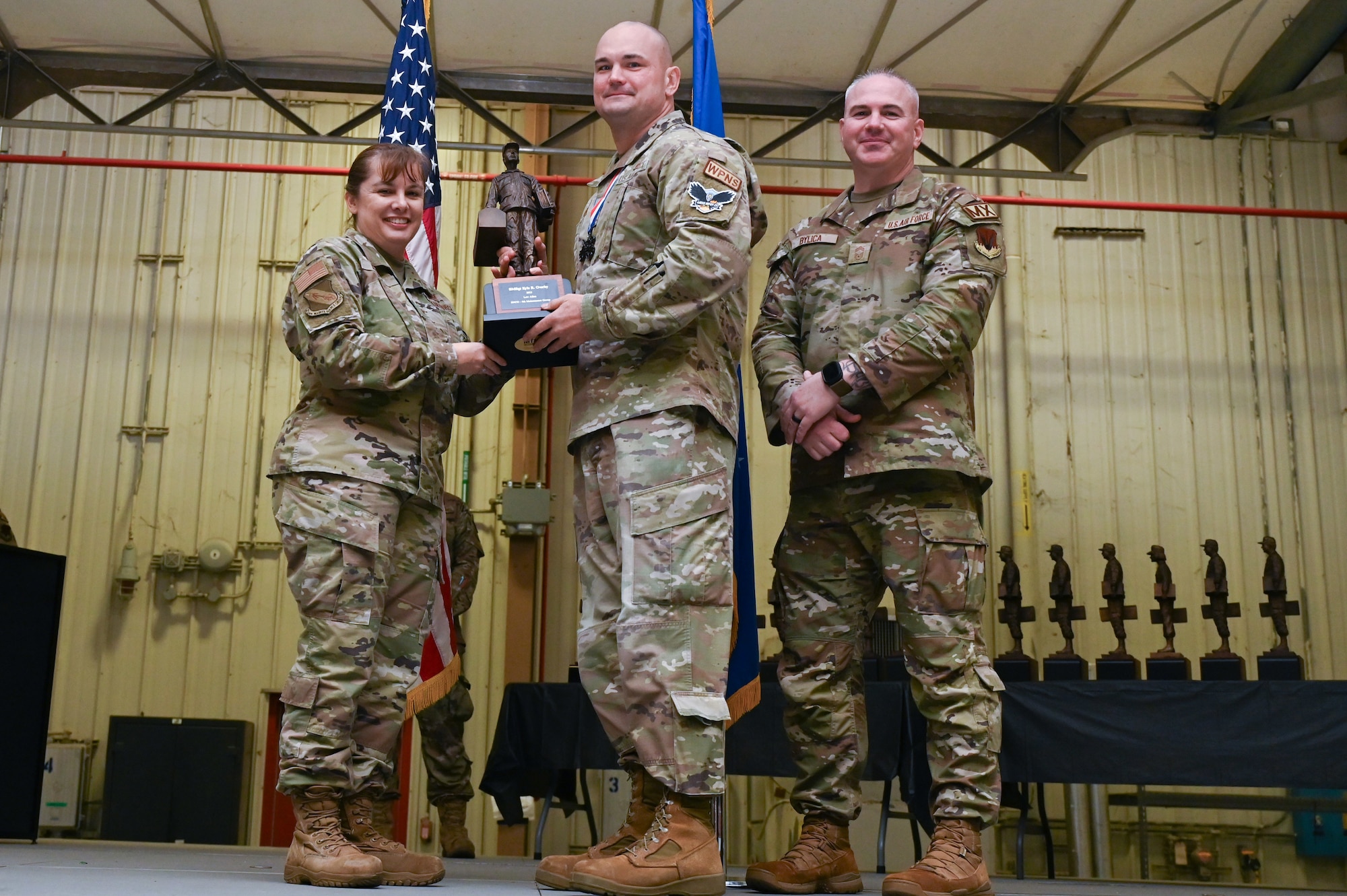 Senior Master Sgt. Kyle Overby, center, assigned to the 336th Fighter Generation Squadron, receives the General Lew Allen award from Col. Kathryn Roman, 4th Maintenance Group commander and Chief Master Sgt. Michael Bylica, 4 MXG senior enlisted leader, during the 4 MXG Maintenance Person of the Year ceremony at Seymour Johnson Air Force Base, North Carolina, Mar. 08, 2024. The 4th Maintenance Group hosts the event annually for MXG Airmen to celebrate their achievements and hard work. (U.S. Air Force photo by Airman Rebecca Tierney)