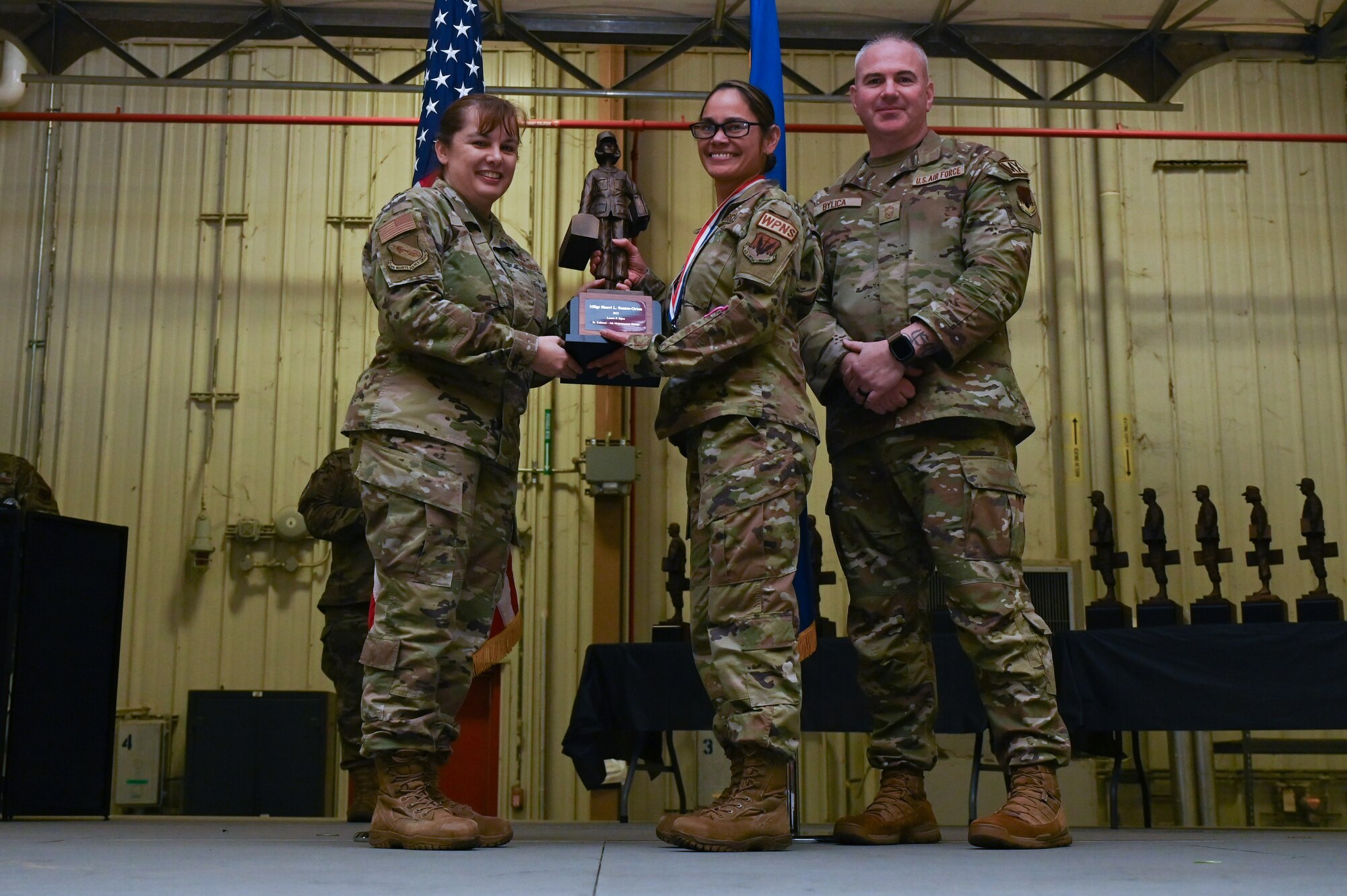 Master Sgt. Sherri Santos, center, assigned to the 334th Fighter Generation Squadron, receives the Lance P. Sijan award from Col. Kathryn Roman, 4th Maintenance Group commander and Chief Master Sgt. Michael Bylica, 4 MXG senior enlisted leader, during the 4 MXG Maintenance Person of the Year ceremony at Seymour Johnson Air Force Base, North Carolina, Mar. 08, 2024. The 4th Maintenance Group hosts the event annually for MXG Airmen to celebrate their achievements and hard work. (U.S. Air Force photo by Airman Rebecca Tierney)