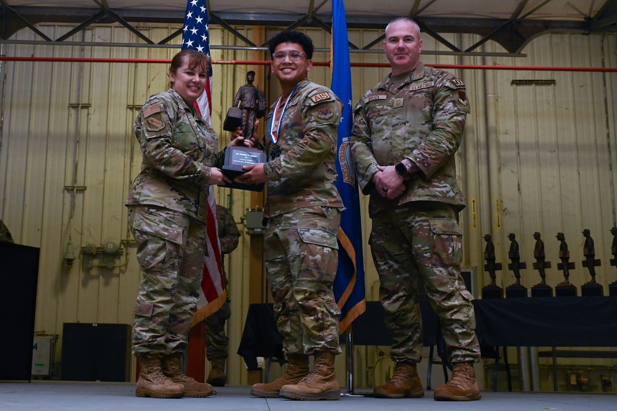 Senior Airman Jonathan Capayas, center, assigned to the 4th Component Maintenance Squadron, receives the Lt. General Leo Marquez award from Col. Kathryn Roman, 4th Maintenance Group commander and Chief Master Sgt. Michael Bylica, 4 MXG senior enlisted leader, during the 4 MXG Maintenance Person of the Year ceremony at Seymour Johnson Air Force Base, North Carolina, Mar. 08, 2024. The 4th Maintenance Group hosts the event annually for MXG Airmen to celebrate their achievements and hard work. (U.S. Air Force photo by Airman Rebecca Tierney)