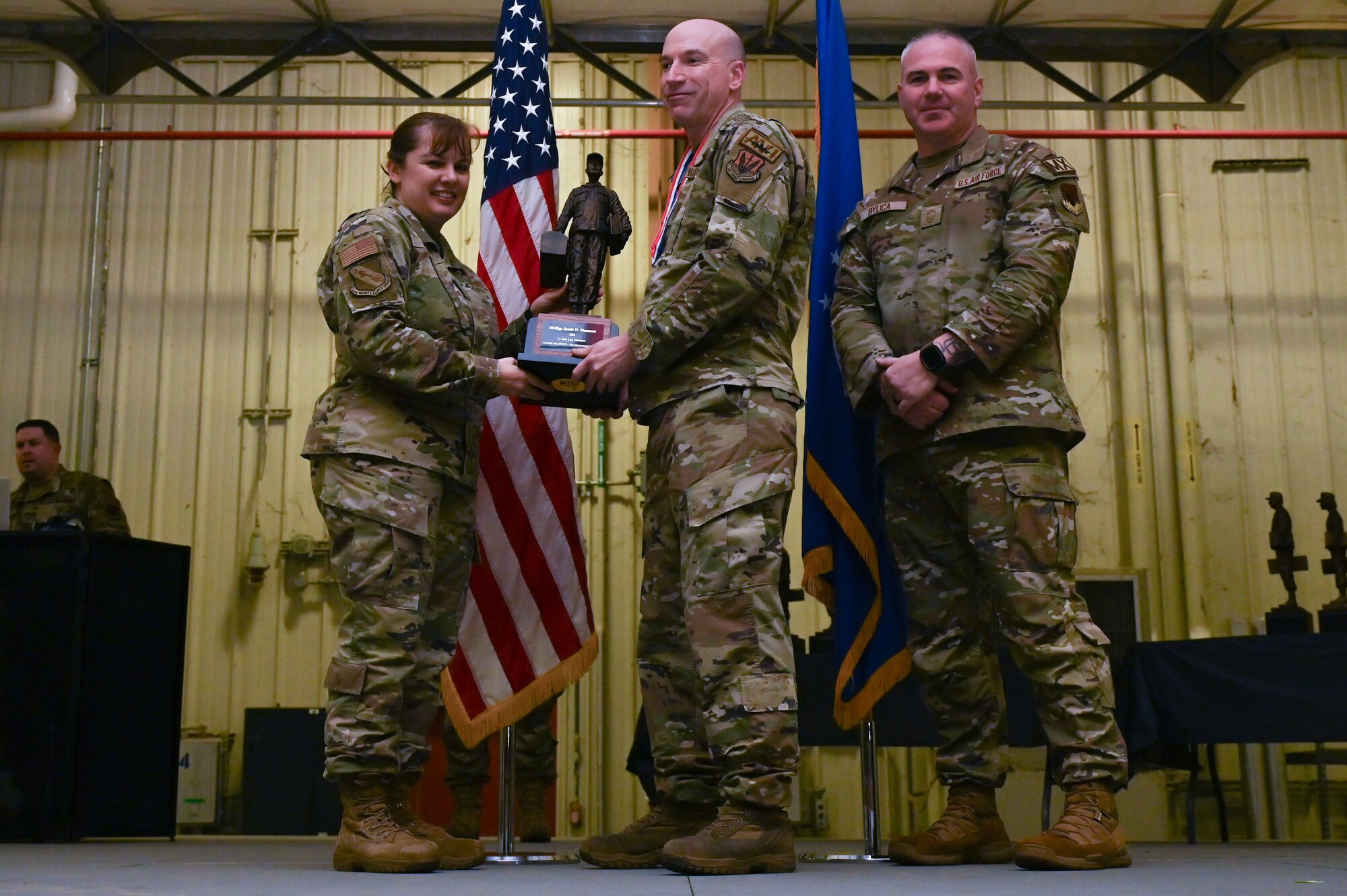 Senior Master Sgt. Jessie Simmons, center, assigned to the 335th Fighter Generation Squadron, receives the Lt. General Leo Marquez award from Col. Kathryn Roman, 4th Maintenance Group commander and Chief Master Sgt. Michael Bylica, 4 MXG senior enlisted leader, during the 4 MXG Maintenance Person of the Year ceremony at Seymour Johnson Air Force Base, North Carolina, Mar. 08, 2024. The 4th Maintenance Group hosts the event annually for MXG Airmen to celebrate their achievements and hard work. (U.S. Air Force photo by Airman Rebecca Tierney)