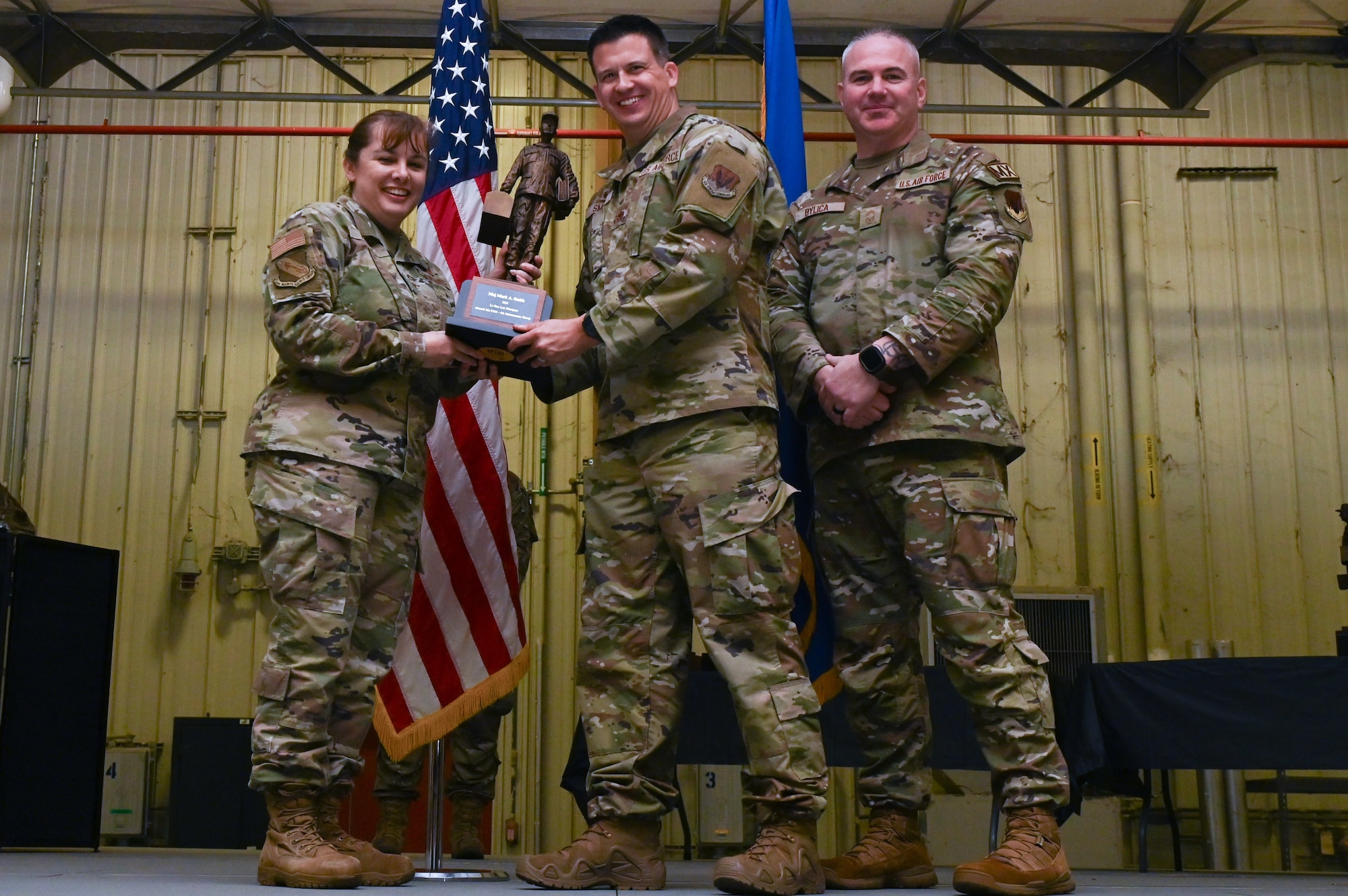 Maj. Mark Smith, center, assigned to the 336th Fighter Generation Squadron, receives the Lt. General Leo Marquez award from Col. Kathryn Roman, 4th Maintenance Group commander and Chief Master Sgt. Michael Bylica, 4 MXG senior enlisted leader, during the 4 MXG Maintenance Person of the Year ceremony at Seymour Johnson Air Force Base, North Carolina, Mar. 08, 2024. The 4th Maintenance Group hosts the event annually for MXG Airmen to celebrate their achievements and hard work. (U.S. Air Force photo by Airman Rebecca Tierney)