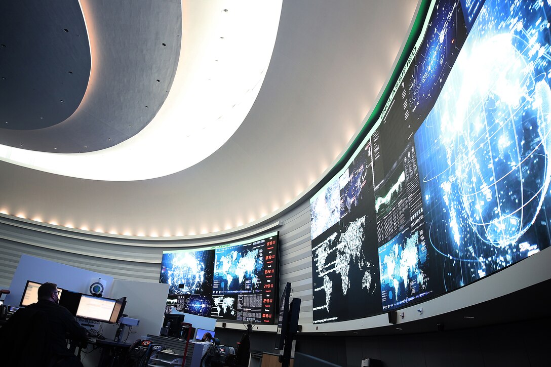 A man in civilian attire sits at a computer terminal on a watch floor.
