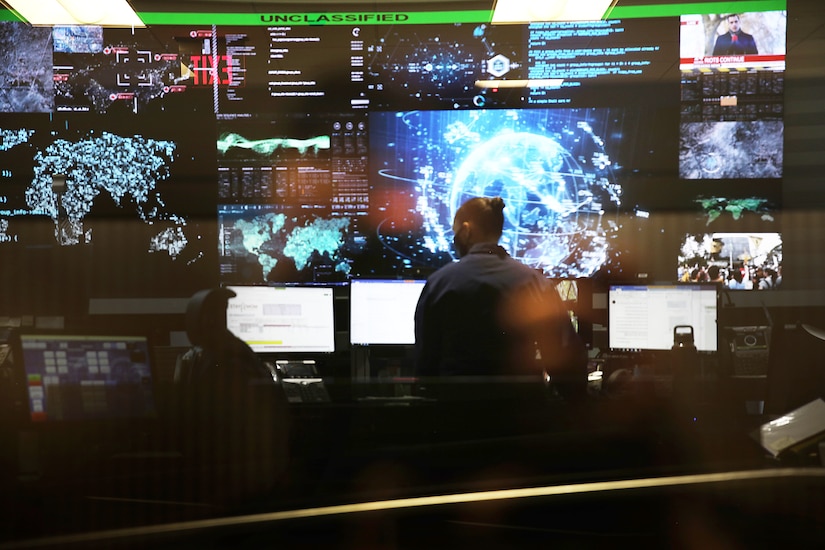 A man in civilian attire stands at a computer terminal on a watch floor.