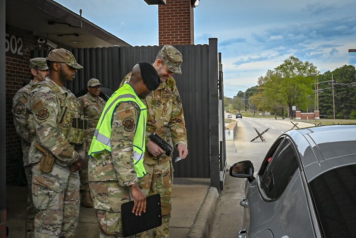 Five Airmen stand at a check in point while one scans an ID.