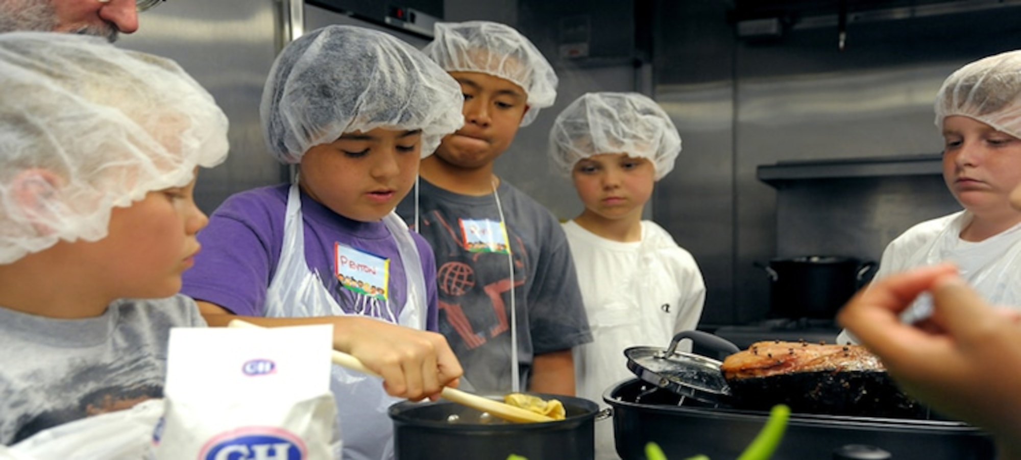 Youth watch another serve food from a pot