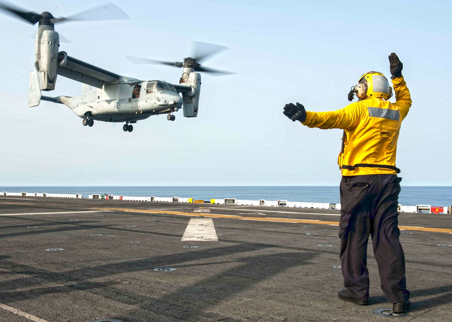 Aviation Boatswain’s Mate (Handling) Airman Fernando Portugal signals to the pilot of an MV-22 Osprey, assigned to Marine Medium Tiltrotor Squadron (VMM) 166 (Reinforced), as it prepares to land on the flight deck of amphibious assault ship USS Boxer (LHD 4). Boxer is the flagship for the Boxer Amphibious Ready Group and, with the embarked 13th Marine Expeditionary Unit, is deployed in support of maritime security operations and theater security cooperation efforts in the U.S. 5th Fleet area of operations.