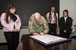 Man in military uniform signing poster with three students looking on