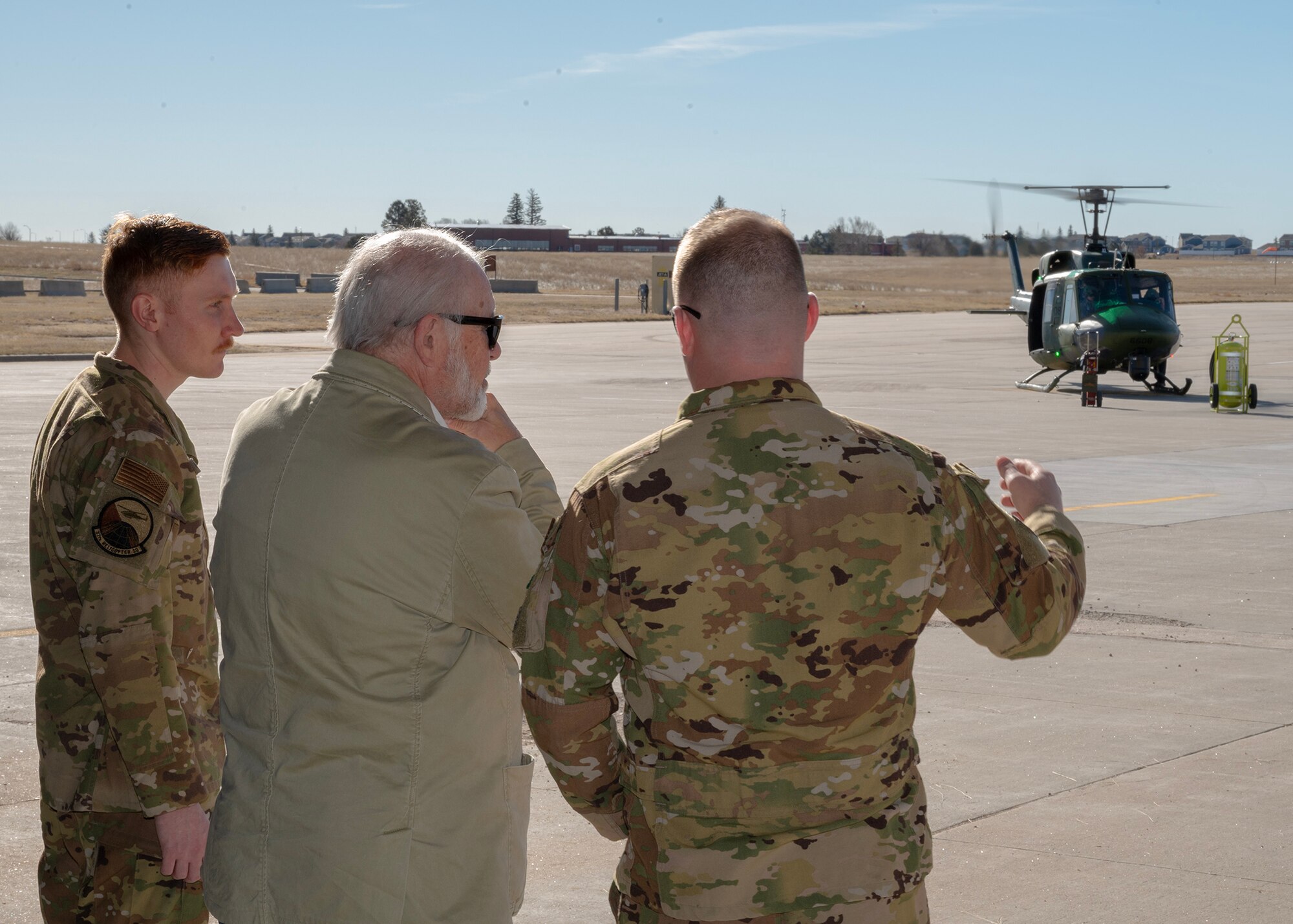 three men looking out hangar bay doors at a helicopter with rotors turning