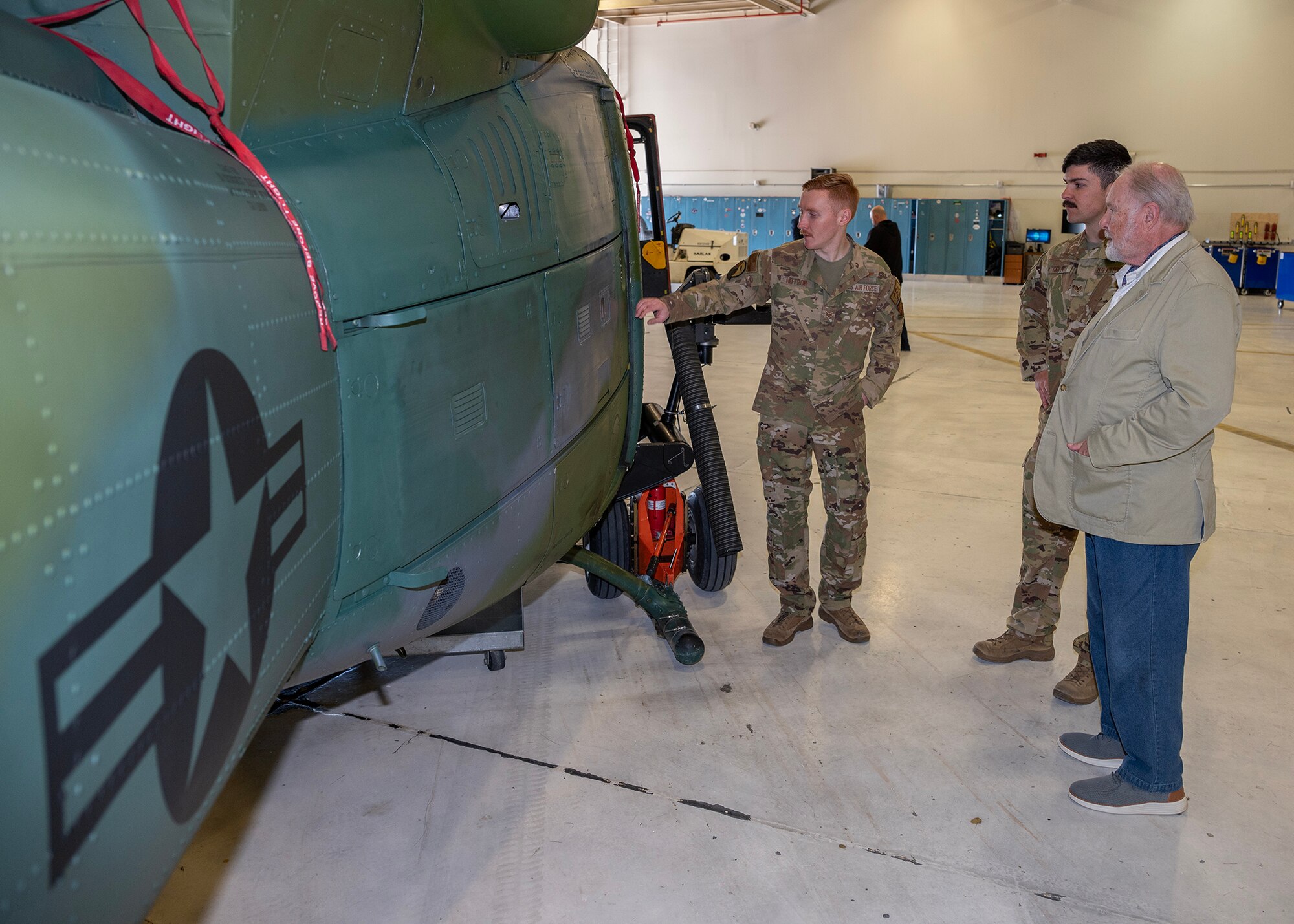 Senior Airman pointing out the inside of a Huey helicopter from the  outside.