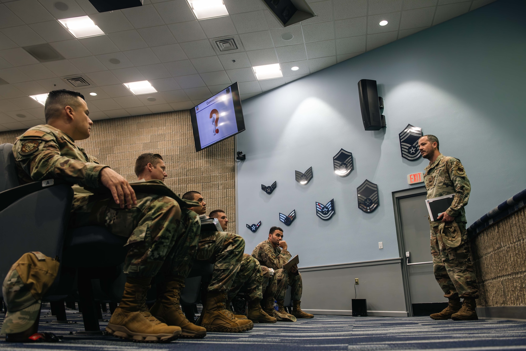 Service members in uniform watch a presentation.