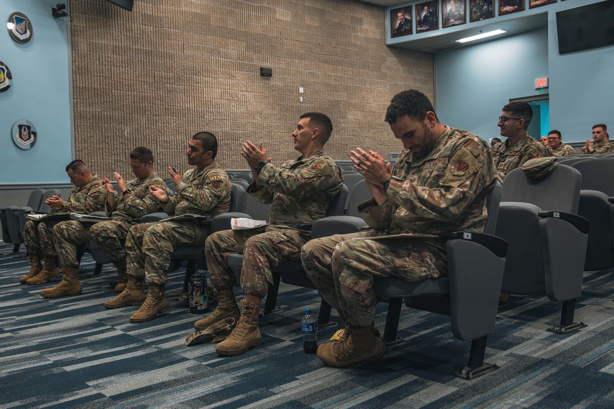 Service Members in the audience of a large auditorium clap for presenters.