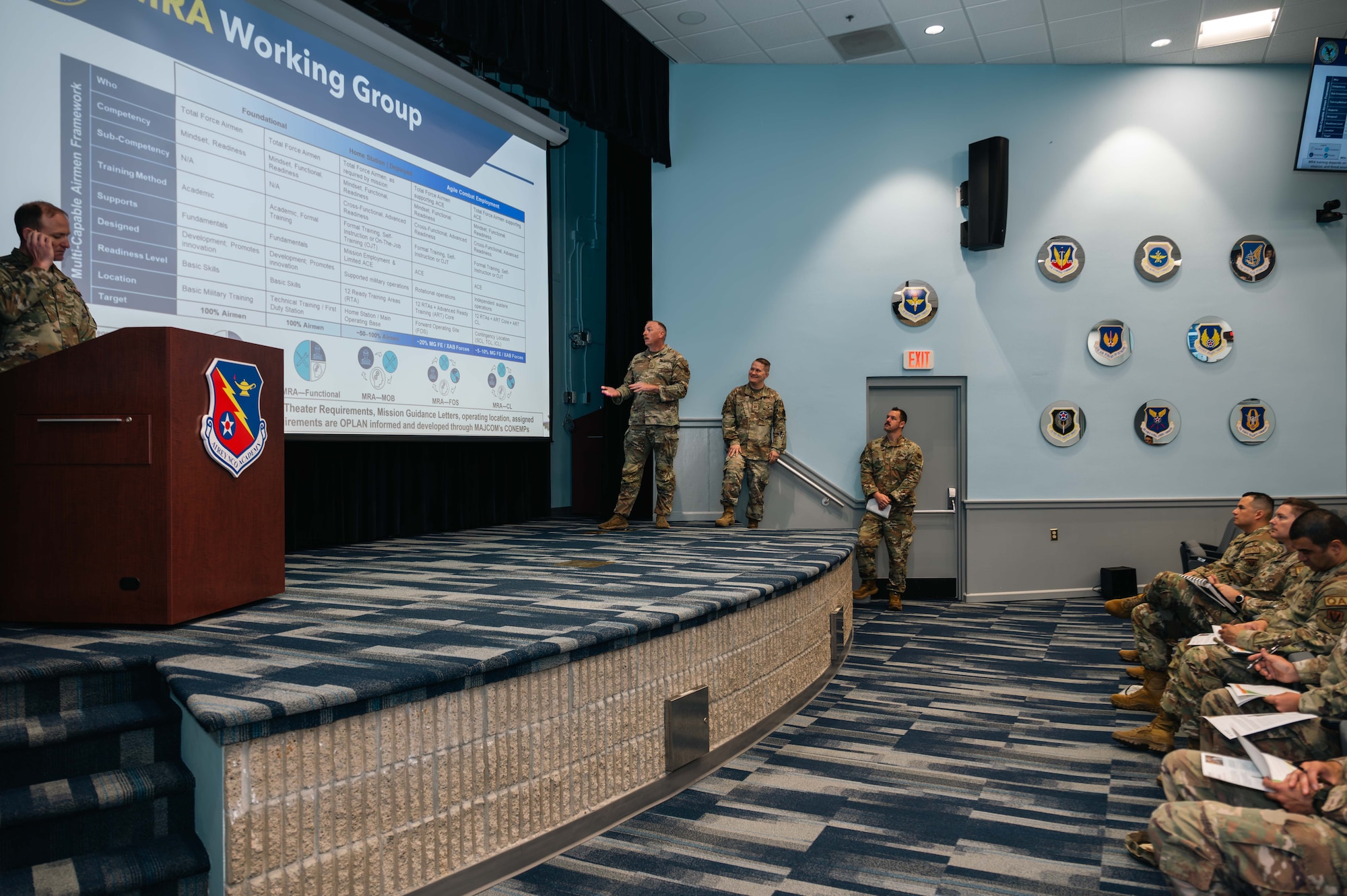 Service members in uniform giving a presentation on stage.