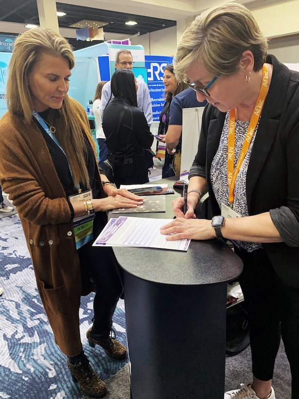 Two women stand at a tall table, one looking down at a piece of paper.