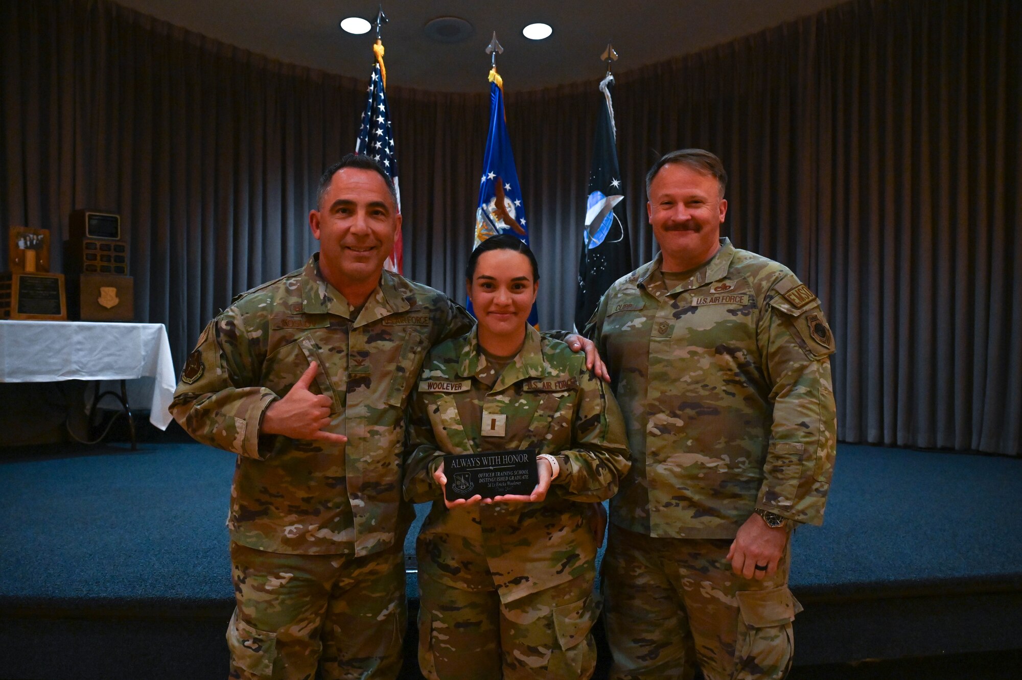 U.S. Air Force Col. Josh Koslov, 350th Spectrum Warfare Wing commander, left, U.S. Air Force 2nd Lt. Ericka Woolever, U.S. Air Force Officer Training School trainee, center, and U.S. Air Force Chief Master Sgt. Will Cupp, 350th SWW command chief, right, pose for a photo celebrating Woolever earning the Distinguished Graduate Award at Maxwell Air Force Base, AL, March 28, 2024. The Distinguished Graduate Award is awarded to the top 10% of class members. (U.S. Air Force photo by Capt. Benjamin Aronson)