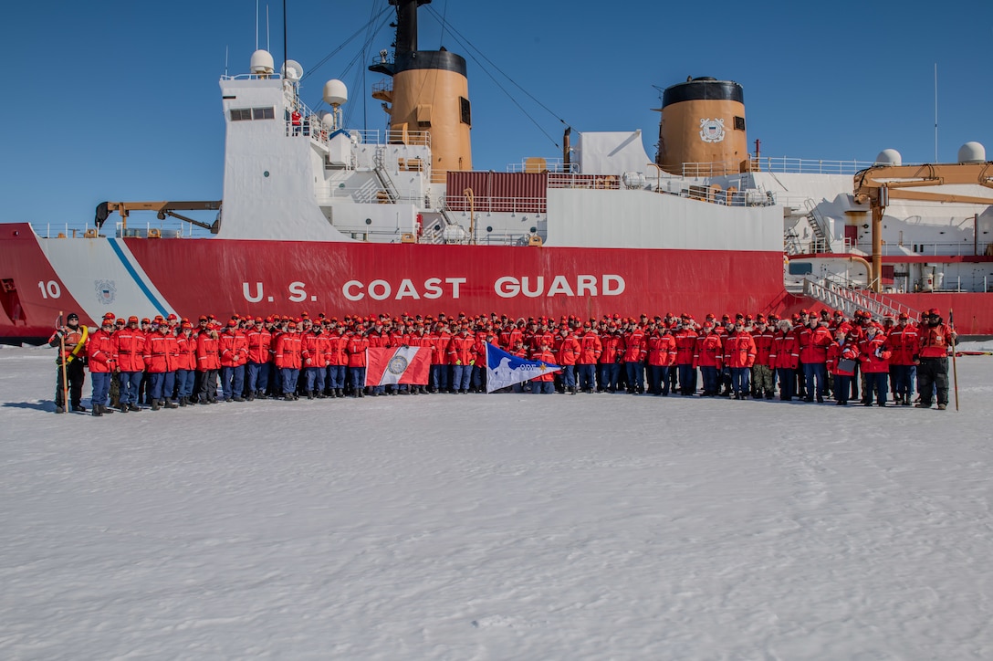 The crew of the U.S. Coast Guard Cutter Polar Star (WAGB 10) stands on the ice in front of the cutter in McMurdo Sound, Antarctica, Dec. 29, 2023. Every year, a joint and total force team works together to complete a successful Operation Deep Freeze season. Active, Guard, and Reserve service members from the U.S. Air Force, Army, Coast Guard, and Navy work together to forge a strong JTF-SFA that continues the tradition of U.S. military support to the United States Antarctic Program. (U.S. Coast Guard photo by Petty Officer 3rd Class Ryan Graves)