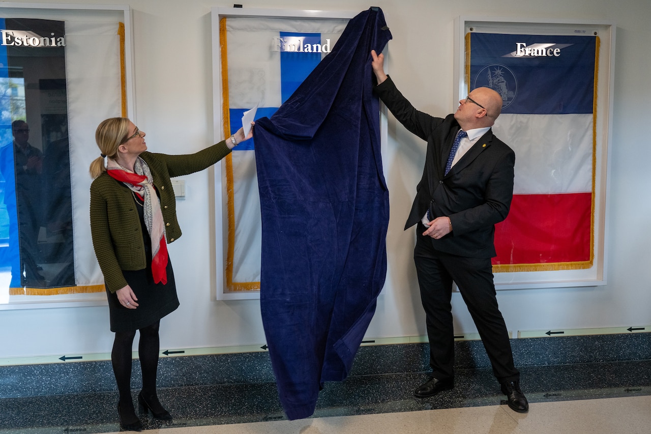 Two civilians uncover a foreign flag hanging on a wall.