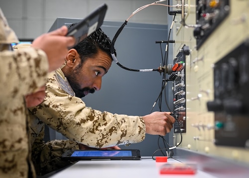 Man plugs a wire into a wall with other wires.