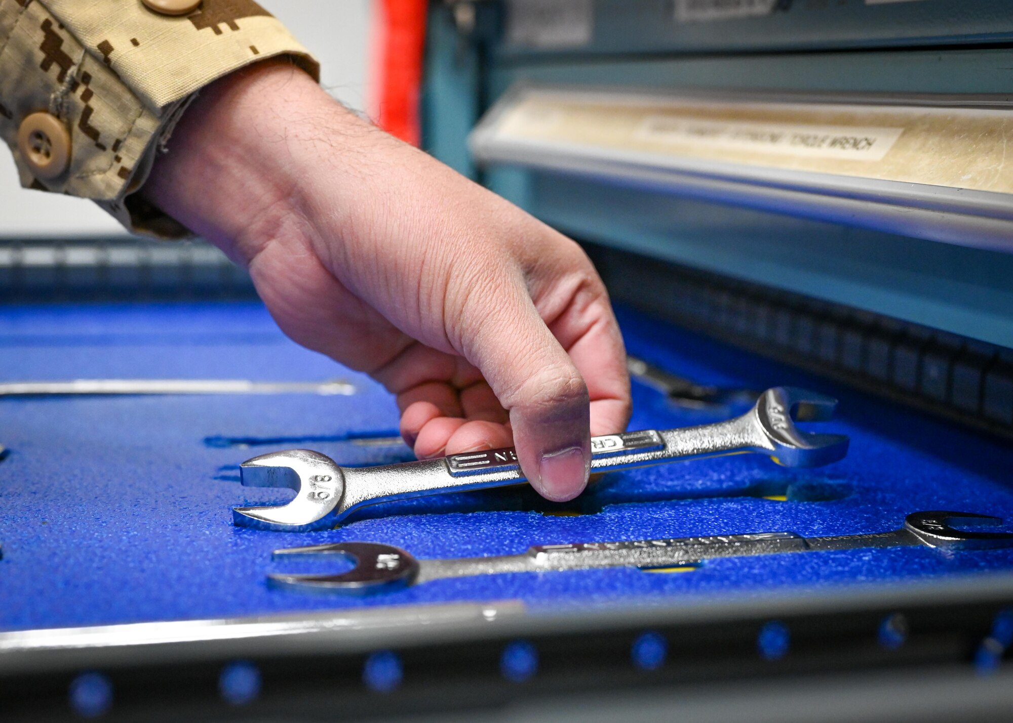 A close-up of a hand picking up a wrench from a tool box.
