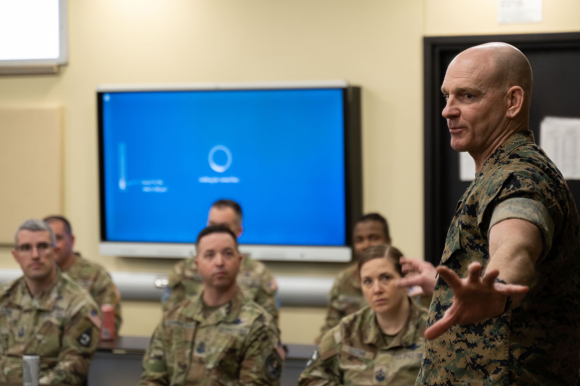 A military member standing in a room talking to other military members.