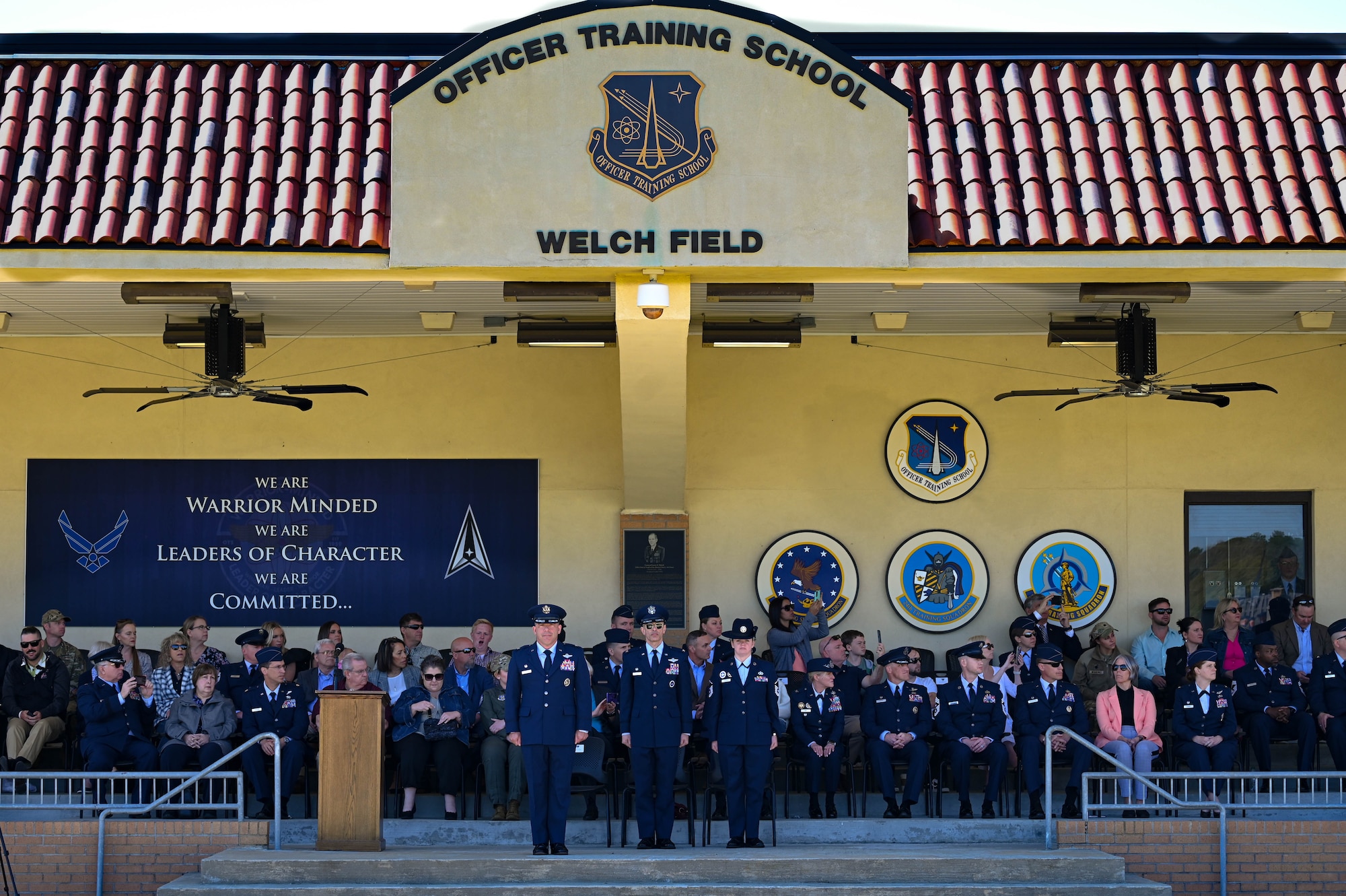 U.S. Air Force Col. Josh Koslov, 350th Spectrum Warfare Wing commander, left, U.S. Air Force Col. Derrick Iwaneko, U.S. Air Force Officer Training School commandant, center, and U.S. Air Force Master Sgt. Candice Davis, OTS training instructor, stand at attention during the OTS graduation parade at Maxwell Air Force Base, AL, March 28, 2024. The program consists of 30 hours of pre-requisite distance learning and eight weeks of military training and leadership development for college graduates. (U.S. Air Force photo by Capt. Benjamin Aronson)
