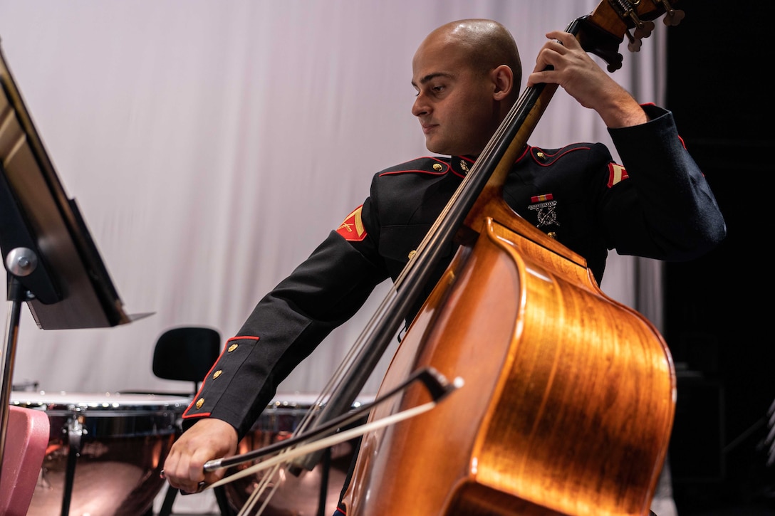 A Marine in a formal uniform plays the upright bass while looking at a music stand.