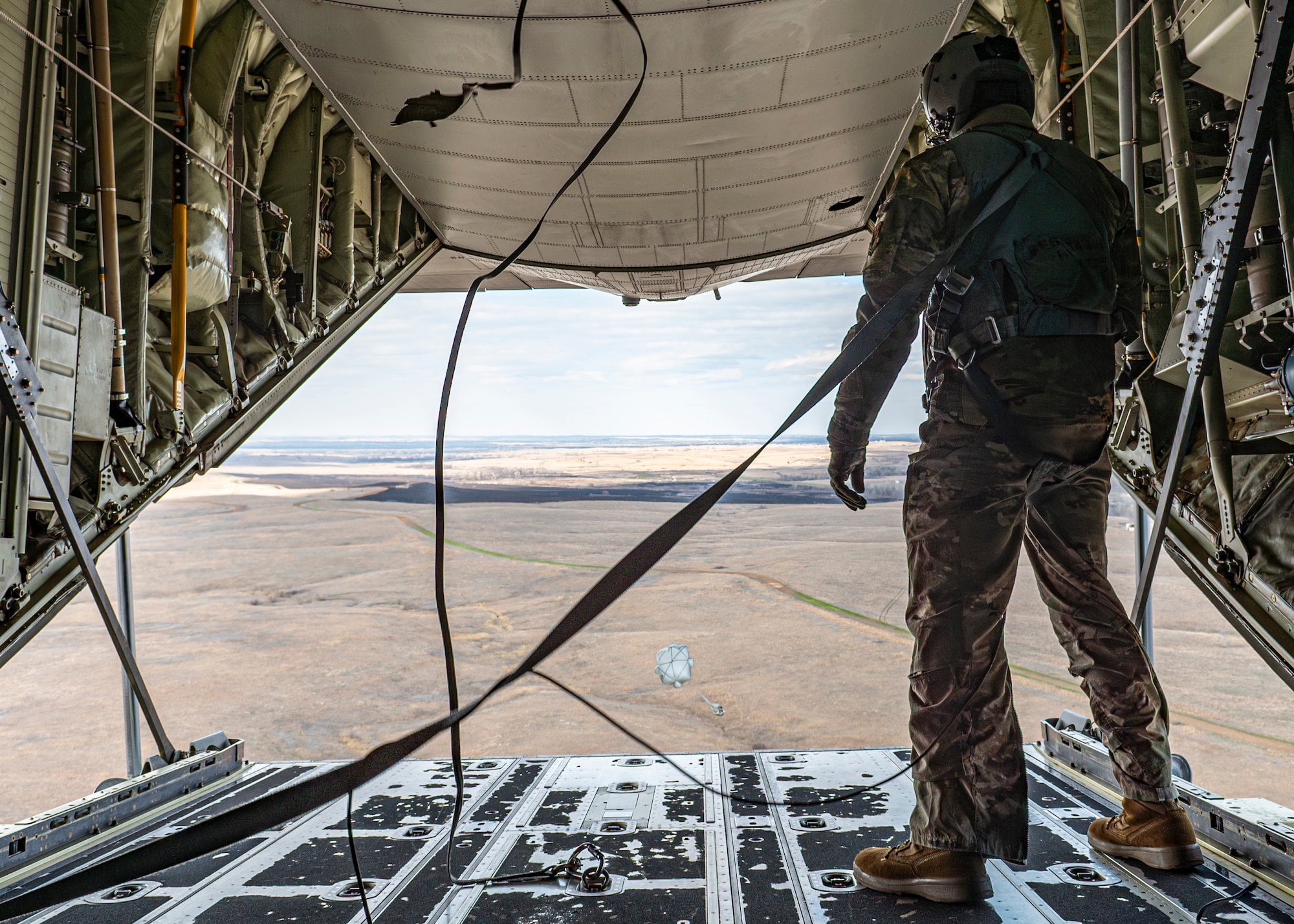 U.S. Air Force Airman 1st Class Erick Fuentes, 71st Rescue Squadron loadmaster, watches cargo descend to the ground from an HC-130J Combat King II over Salina Regional Airport, Kansas, March 27, 2024. The aerial cargo drop was part of the Rescue Rodeo, a rescue training event and competition. Airmen had to account for plane speed, winds, and altitude when performing the precision drops. (U.S. Air Force photo by Airman 1st Class Leonid Soubbotine)