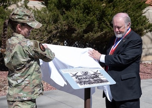 general in uniform and state senator in black suit pull a white cover off a sign.