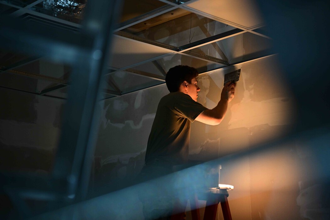 Senior Airman applies a layer of drywall mud to a building