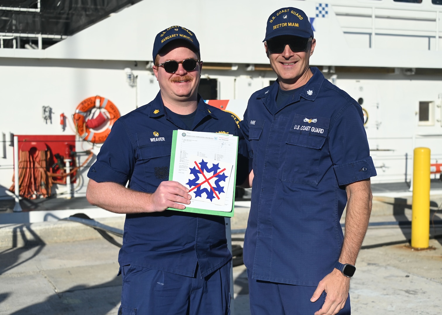 Cmdr. Eric Pare, Coast Guard Sector Miami chief of response, presents a snowflake with an "X" emblem to Lt. Cmdr. Colin Weaver, commanding officer of USCGC Margaret Norvell (WPC 1105), at Coast Guard Base Miami Beach, April 5, 2024. The cutter received the snowflake emblem for carrying out a successful drug interdiction. (U.S. Coast Guard photo by Petty Officer 2nd Class Diana Sherbs)