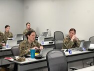 Woman in Air Force uniform appears to be asking a question while gesturing towards her computer in a classroom with other military members