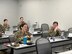 Woman in Air Force uniform appears to be asking a question while gesturing towards her computer in a classroom with other military members