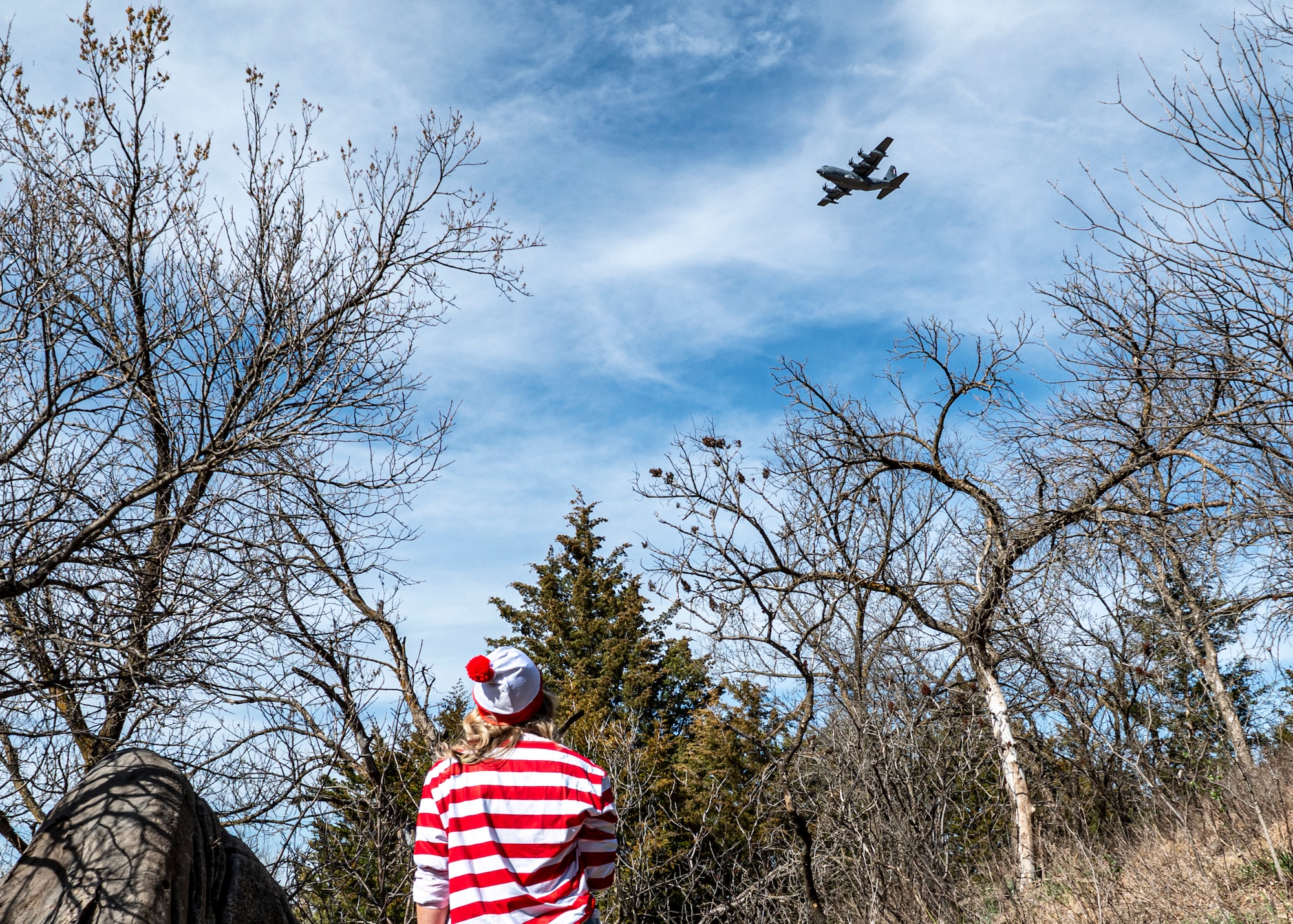U.S. Air Force Staff Sgt. Stacy Robinson, 23rd Wing A-Staff, watches an HC-130J Combat King II fly overhead at Mushroom Rock State Park, Kansas, March 28, 2024. As part of the Rescue Rodeo competition, rescue units took turns searching for Robinson from inside the aircraft. (U.S. Air Force photo by Airman 1st Class Leonid Soubbotine)