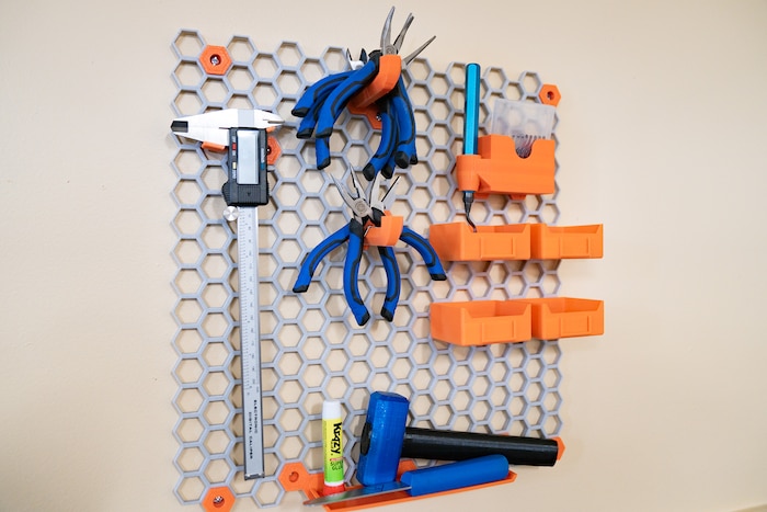 Colorful blue and orange tools hang from a mesh hexagonal structure from a wall.