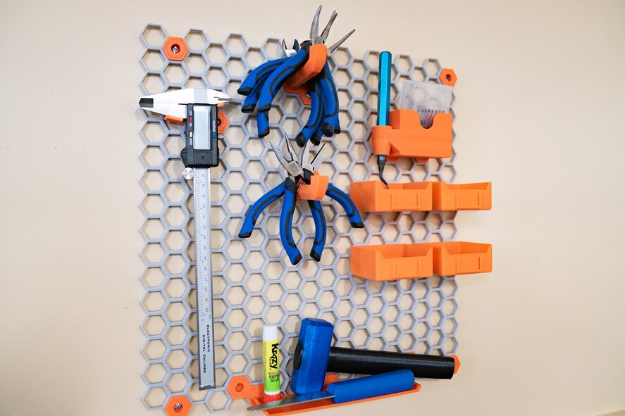 Colorful blue and orange tools hang from a mesh hexagonal structure from a wall.