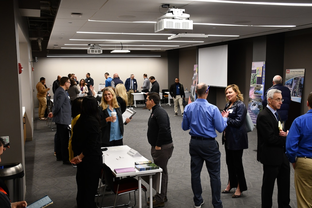 Group of business professionals in a large room stand and discuss engineering topics