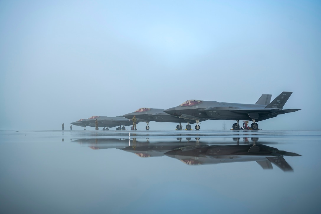 Three parked jets are surrounded by fog are mirrored on a flight line.