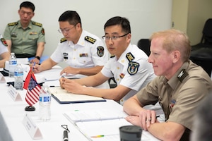 Service members in U.S. and foreign military uniforms sit at table displaying U.S. and Chinese flags.
