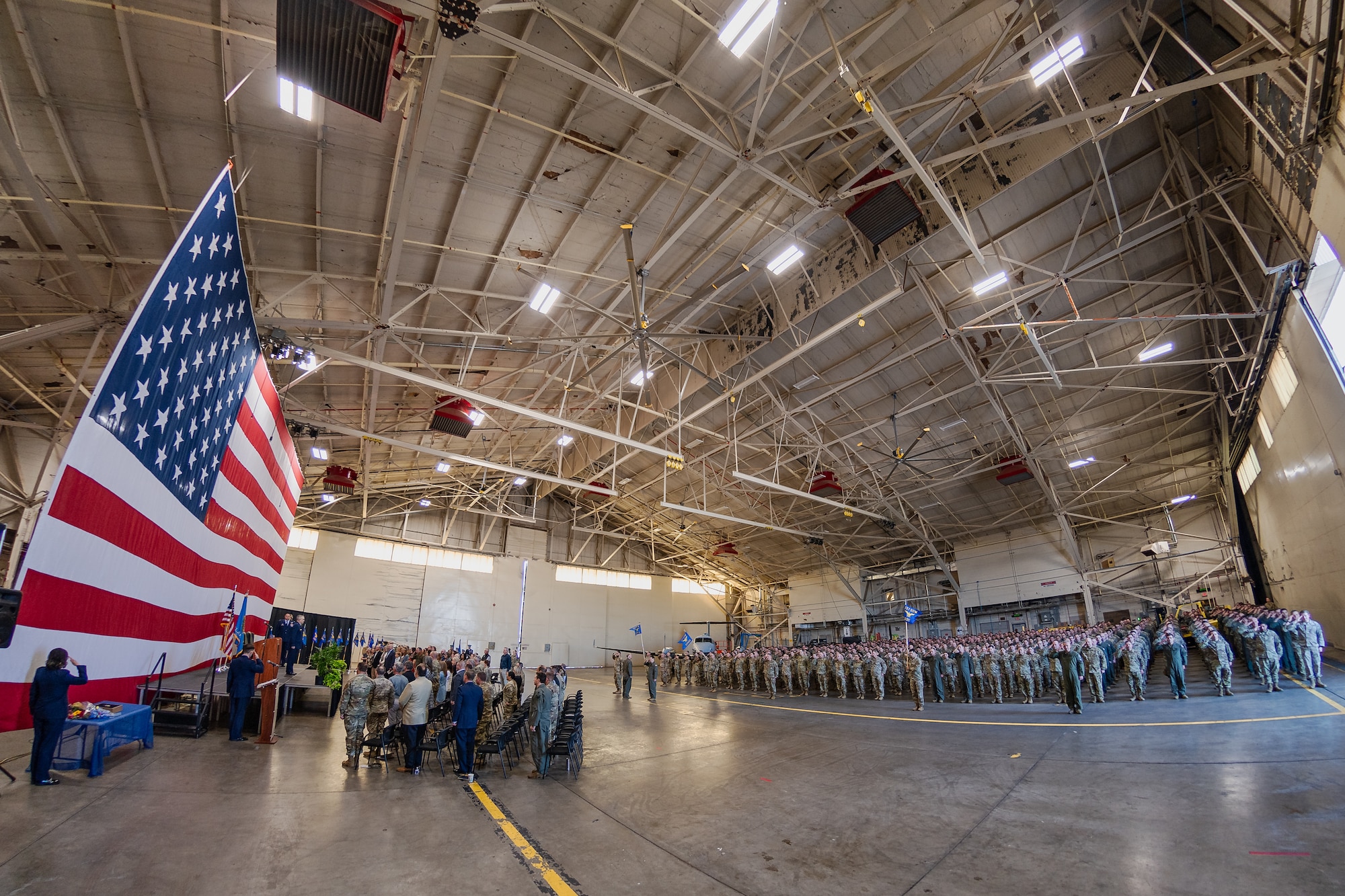 A crowd of Airmen gather in formation for a change of command ceremony in an aircraft hangar