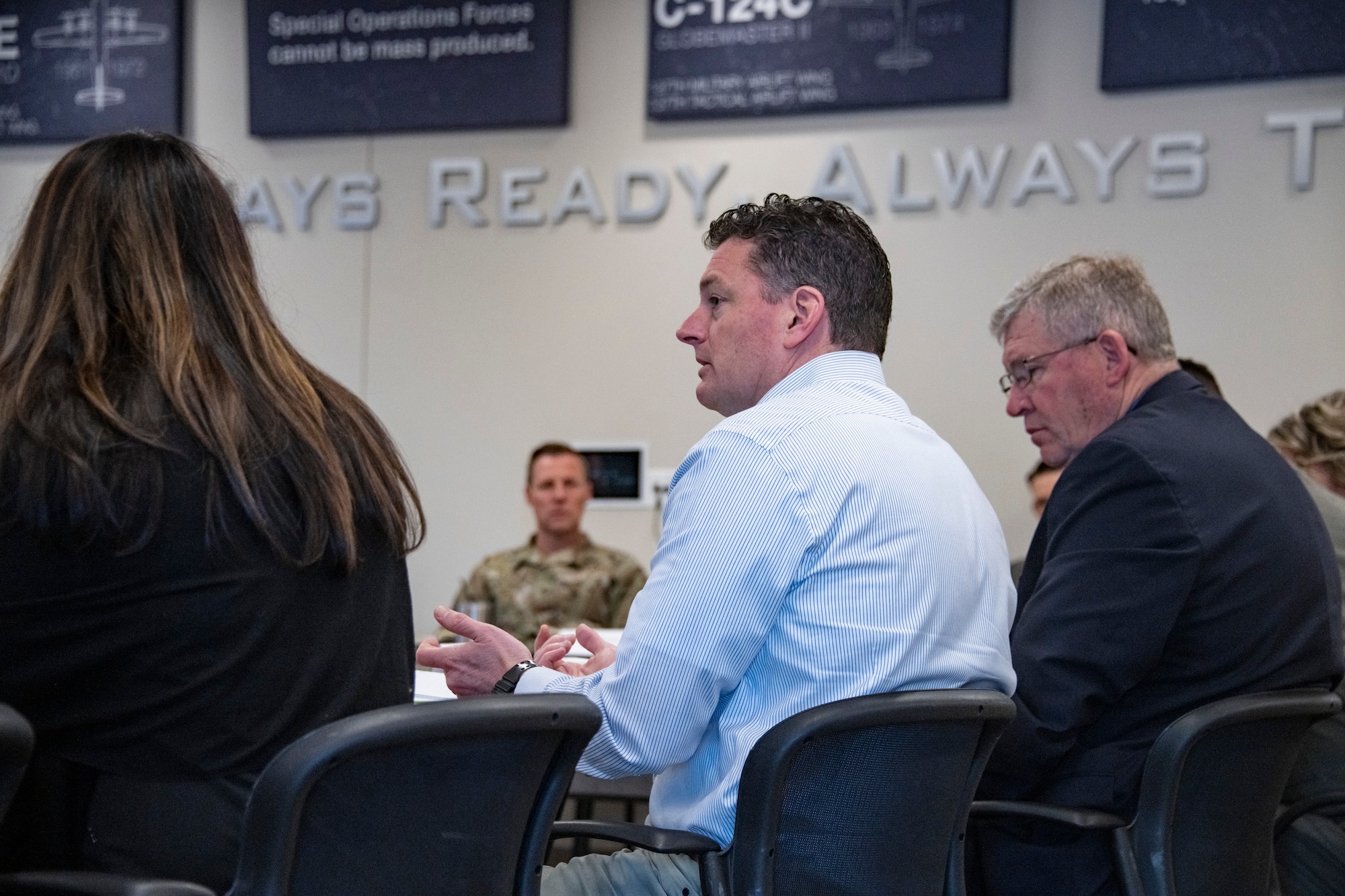 The Assistant Secretary of Defense for Special Operations and Low-Intensity Conflict participates in a presentation with other officials in business attire and Airmen in OCPs