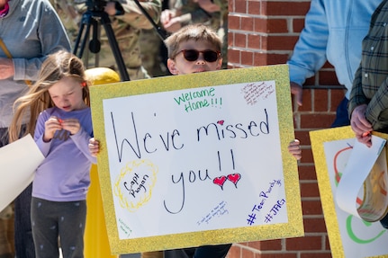A photo of a child holding a welcome home sign.