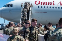 A photo of Airmen walking down stairs from an aircraft and being greeted by other Airmen.
