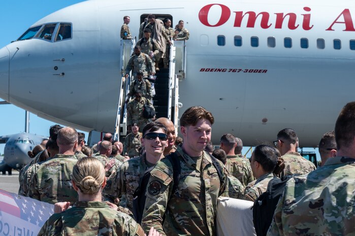 A photo of Airmen walking down stairs from an aircraft and being greeted by other Airmen.