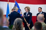 U.S. Air Force female colonel takes guidon from U.S. Air Force male general in dress uniforms in front of crowd