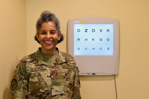Major Leslie Wilson stand in her office next to an eye exam chart.