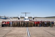 A large crowd of people stand on the flightline in front of several aircraft