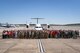 A large crowd of people stand on the flightline in front of several aircraft